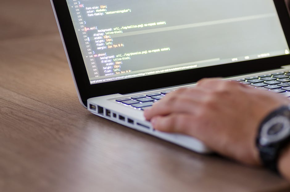A close-up shot of a laptop screen displaying lines of code, with a ceramic mug placed beside it on a wooden surface. The mug features text about coffee, suggesting a casual or work environment. The b
